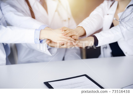 Group of doctors joining hands as a circle and ready to help patients while sitting at the desk in modern hospital office. Successful teamwork in medicine, Coronavirus countering concept 73516438
