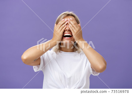 Can I look now. Portrait of excited pleased attractive tanned girlfriend in white t-shirt closing eyes and smiling broadly waiting for boyfriend bring surprising gift over purple background 73516978