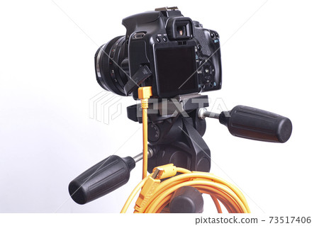 Digital photo camera on black tripod with orange rolled cable Digital photo camera on black tripod with orange rolled cable 73517406