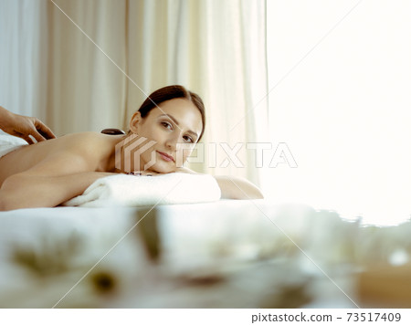 Pretty brunette woman enjoying treatment with hot stones in spa salon. Beauty concept Pretty brunette woman enjoying treatment with hot stones in spa salon. Beauty concept 73517409