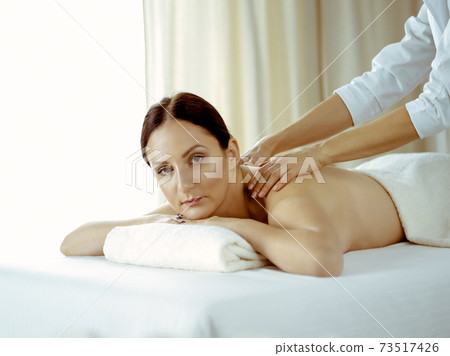 Pretty brunette woman enjoying procedure of back massage in spa salon. Beauty concept 73517426
