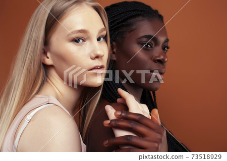 two pretty girls african and caucasian blond posing cheerful together on brown background, ethnicity diverse lifestyle people concept two pretty girls african and caucasian blond posing cheerful together on brown background, ethnicity diverse lifestyle people concept 73518929