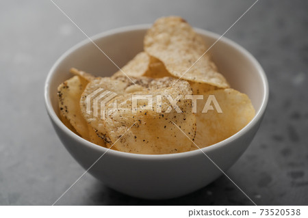 White bowl with organic potato chips sprinkled with fresh ground black pepper on concrete background 73520538