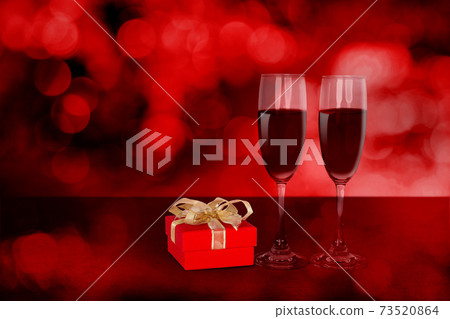 Two wineglasses and red gift box on desk with red blur bokeh background. Two wineglasses and red gift box on desk with red blur bokeh background. 73520864