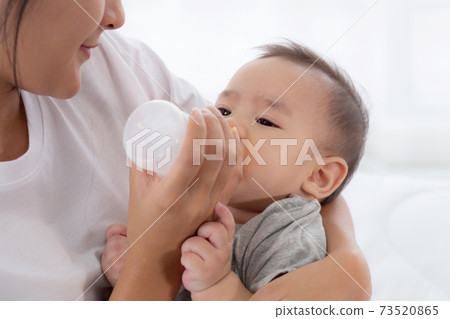 Young asian mother embracing and feeding little baby girl with bottle of milk at home. Young asian mother embracing and feeding little baby girl with bottle of milk at home. 73520865