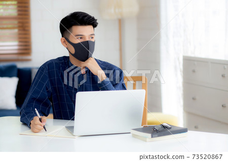 Young business man in face mask planning and working from home on laptop computer on desk. Young business man in face mask planning and working from home on laptop computer on desk. 73520867