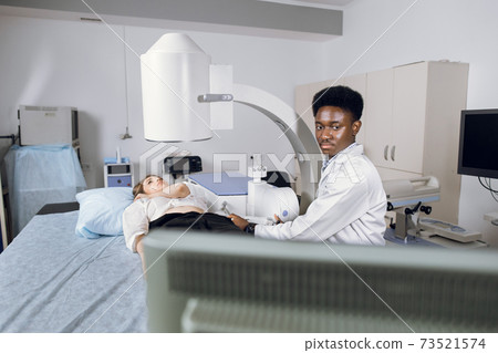 Lithotripsy for kidney and ureteral stones in modern center. Professional African man doctor, using ultrasound scan to determine the stone position before the lithotripsy for his female patient Lithotripsy for kidney and ureteral stones in modern center. Professional African man doctor, using ultrasound scan to determine the stone position before the lithotripsy for his female patient 73521574