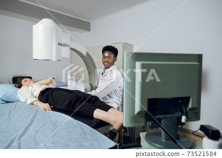 Extracorporeal Shock Wave Therapy. Kidney stone treatment. African man doctor looking at the digital screen of the lithotriptor to determine kidney stones position of his female patient Extracorporeal Shock Wave Therapy. Kidney stone treatment. African man doctor looking at the digital screen of the lithotriptor to determine kidney stones position of his female patient 73521584