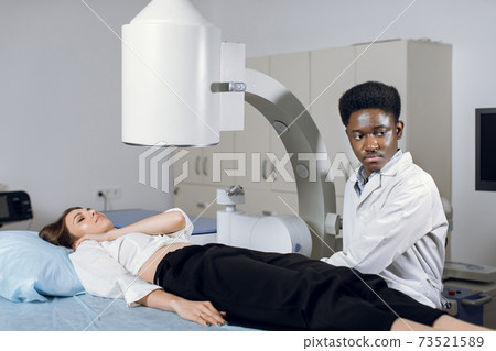Young high-skilled focused black man doctor in white coat, providing lithotripsy procedure for his lying female patient with modern ultrasonic lithotriptor to break up stones Young high-skilled focused black man doctor in white coat, providing lithotripsy procedure for his lying female patient with modern ultrasonic lithotriptor to break up stones 73521589