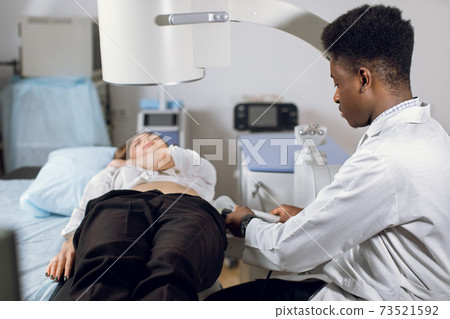 Treatment of urethral stones by non-invasive extracorporeal shock wave lithotripsy. Professional black man doctor working with modern lithotripter to break up stones for his female patient Treatment of urethral stones by non-invasive extracorporeal shock wave lithotripsy. Professional black man doctor working with modern lithotripter to break up stones for his female patient 73521592