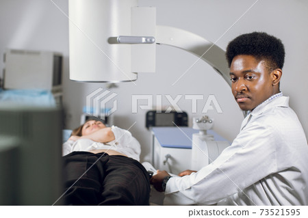 Treatment of urethral stones by non-invasive extracorporeal shock wave lithotripsy. Black man doctor working with modern lithotripter to crush kidney stones for his female patient in modern clinic 73521595