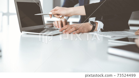 Unknown businessmen and woman sitting, working and discussing questions at meeting in modern office, close-up Unknown businessmen and woman sitting, working and discussing questions at meeting in modern office, close-up 73524499