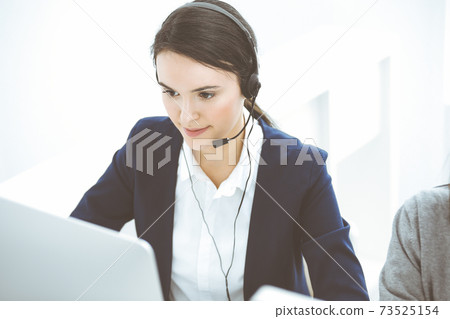 Call center. Beautiful woman sitting and working in headset at customer service office. Business concept Call center. Beautiful woman sitting and working in headset at customer service office. Business concept 73525154