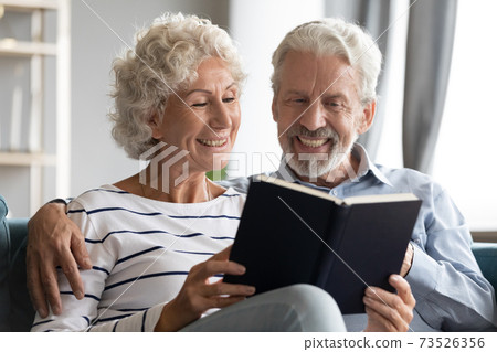 Happy bonding elderly senior retired family couple reading paper book. Happy bonding elderly senior retired family couple reading paper book. 73526356