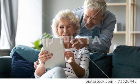 Emotional joyful middle aged senior family couple using digital tablet. 73526445