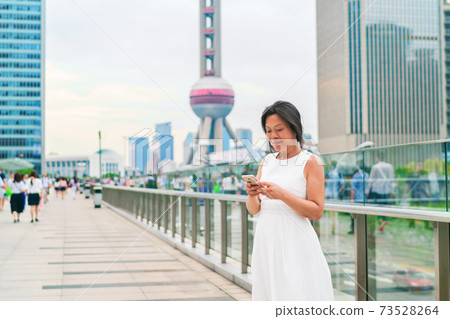 Phone Asian middle aged elegant woman using smartphone texting on Shanghai city street. Mature people lifestyle. Businesswoman holding mobile phone working. Smiling mature businesswoman in China Phone Asian middle aged elegant woman using smartphone texting on Shanghai city street. Mature people lifestyle. Businesswoman holding mobile phone working. Smiling mature businesswoman in China 73528264