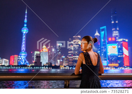 Shanghai city night lights glowing in dark sky. Elegant lady by the Bund river in fancy lace dress evening gown. Asian model sightseeing. 73528271