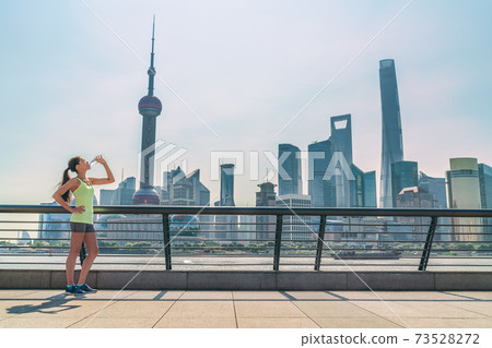 Shanghai skyline fitness woman thirsty drinking water bottle on sunny day, China. Asian jogger thirst quenching drink 73528272