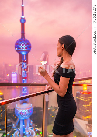 Luxury lifestyle Shanghai city Asian woman drinking white wine glass at rooftop bar party night rich club vip nightclub. Elegant rich lady looking at skyline glowing pearl tv tower in sunset. 73528273