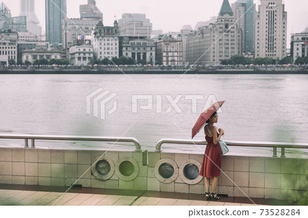 Shanghai city bund river Asian woman walking under rain with umbrella on China Asia vacation. Elegant chinese tourist lady in red dress 73528284