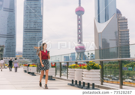 Business woman walking using phone commuting to work in Shanghai city, China. Tourist travel lifestyle Asian lady city street walk, cityscape in summer. View of Pearl Tower during morning commute Business woman walking using phone commuting to work in Shanghai city, China. Tourist travel lifestyle Asian lady city street walk, cityscape in summer. View of Pearl Tower during morning commute 73528287