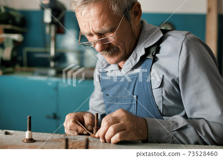 An old master with glasses works in a workshop An old master with glasses works in a workshop 73528460