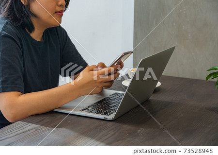 Asian woman using smartphone and laptop on coffee table Asian woman using smartphone and laptop on coffee table 73528948