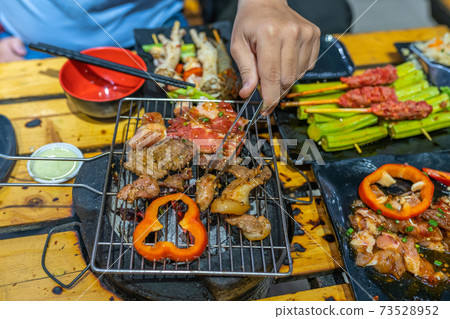 Human hand using tongs while grilling meat and bell pepper Human hand using tongs while grilling meat and bell pepper 73528952