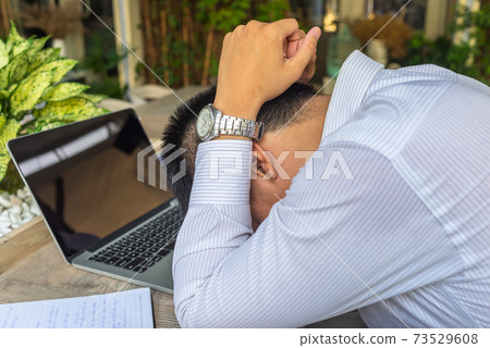 Frustrated Asian businessman holding head while working on laptop 73529608
