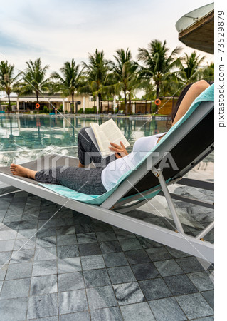 Asian woman reading good book at swimming pool on vacation Asian woman reading good book at swimming pool on vacation 73529879