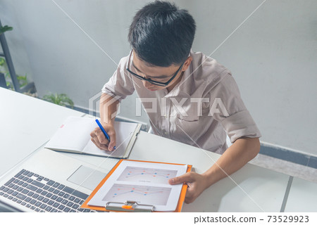 Young Asian businessman writing in a notebook Young Asian businessman writing in a notebook 73529923