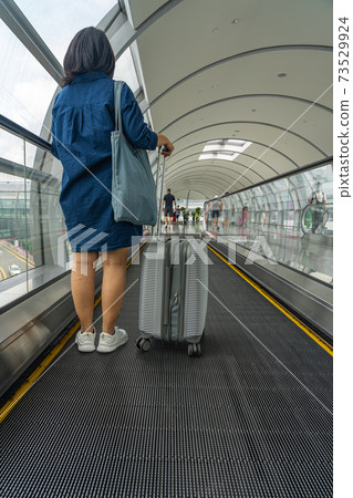 Young female traveler carrying luggage on moving walkway at airport Young female traveler carrying luggage on moving walkway at airport 73529924