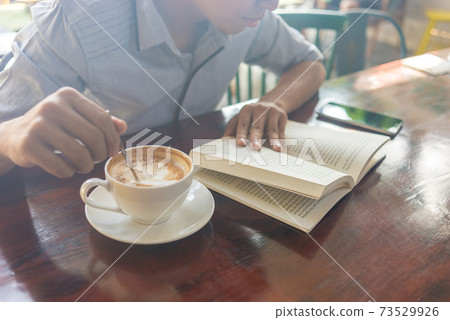 Human hand holding opened book and stir coffee Human hand holding opened book and stir coffee 73529926