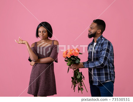 Unwanted confession. Displeased black woman rejecting her admirer with roses on Valentine's Day over pink background 73530531