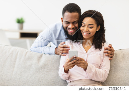 African american couple sitting on couch, using cellphone African american couple sitting on couch, using cellphone 73530841