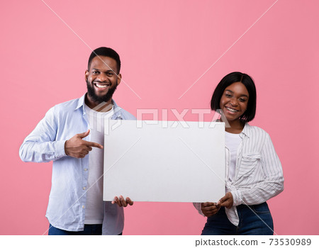 Joyful black couple holding and pointing at empty advertising board with copyspace on pink background, mockup for design Joyful black couple holding and pointing at empty advertising board with copyspace on pink background, mockup for design 73530989