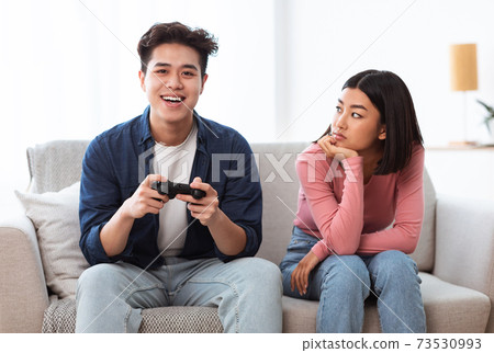 Displeased Japanese Girlfriend Looking At Boyfriend Playing Game At Home Displeased Japanese Girlfriend Looking At Boyfriend Playing Game At Home 73530993