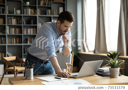 Thoughtful young businessman working on computer standing at table. 73531579