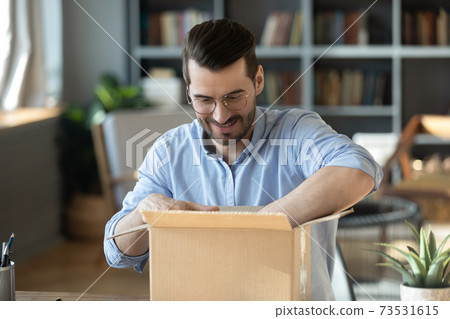 Curious young man in eyeglasses unpacking huge cardboard box. 73531615