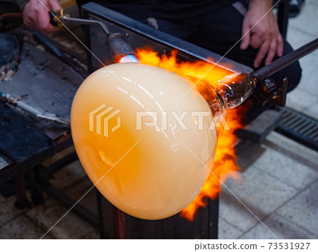 Glass artist forms the scorching glass with heats it with a gas burner Glass artist forms the scorching glass with heats it with a gas burner 73531927