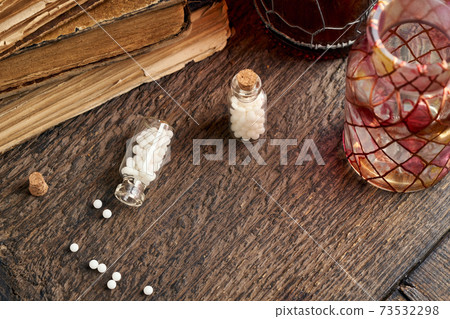 A bottle of homeopathic pills on a wooden table, with vintage books in the background A bottle of homeopathic pills on a wooden table, with vintage books in the background 73532298