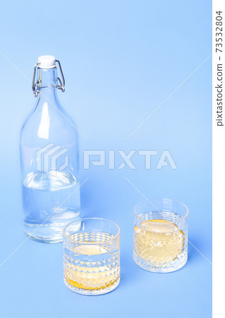 Glass with water and lemon near to bottle on blue background 73532804