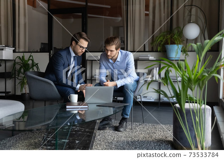 Colleagues using laptop, working on project in modern office together 73533784