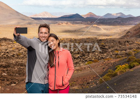 Selfie couple tourists taking self-photo picture with mobile phone on travel vacation. People summer lifestyle woman and man holidaying visiting Lanzarote Timanfaya National Park, Canary Islands Selfie couple tourists taking self-photo picture with mobile phone on travel vacation. People summer lifestyle woman and man holidaying visiting Lanzarote Timanfaya National Park, Canary Islands 73534148