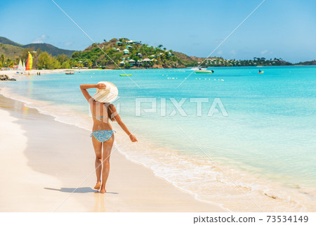 Beach travel vacation woman walking on luxury Caribbean cruise destination Antigua island in bikini wearing beach hat, carefree on holidays on Jolly Beach. Girl on travel vacation holidays swim model Beach travel vacation woman walking on luxury Caribbean cruise destination Antigua island in bikini wearing beach hat, carefree on holidays on Jolly Beach. Girl on travel vacation holidays swim model 73534149