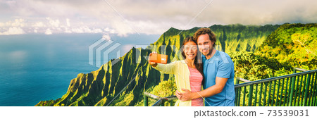 Travel selfie couple at Napali Kauai Hawaii banner. Young tourists at Na Pali Coast lookout taking mobile phone selfie smartphone photo. Travel people at hawaiian landscape, panorama crop Travel selfie couple at Napali Kauai Hawaii banner. Young tourists at Na Pali Coast lookout taking mobile phone selfie smartphone photo. Travel people at hawaiian landscape, panorama crop 73539031
