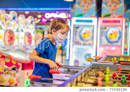 Little blond boy wearing a medical mask during COVID-19 coronavirus playing board table soccer Little blond boy wearing a medical mask during COVID-19 coronavirus playing board table soccer 73540194
