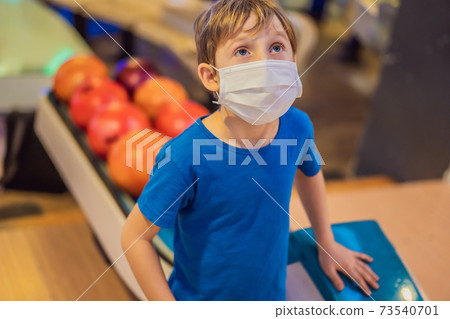 Boy playing bowling with medical masks during COVID-19 coronavirus in bowling club Boy playing bowling with medical masks during COVID-19 coronavirus in bowling club 73540701