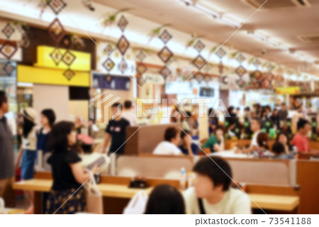 At lunch time, a service area crowded with many people, a landscape / blurred image inside the food court 73541188