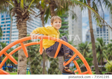 The boy climbs on the playground against the background of palm trees 73541195